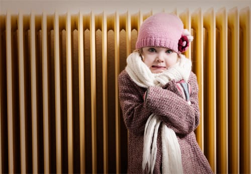 Une petite fille en veste et écharpe devant un radiateur